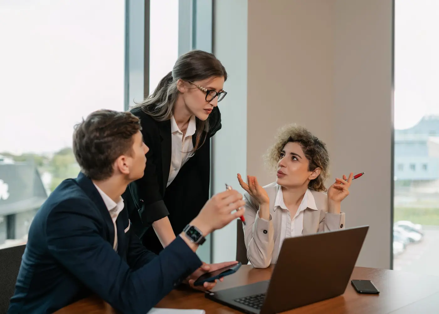 Three colleagues discussing a project around a laptop in a meeting room.